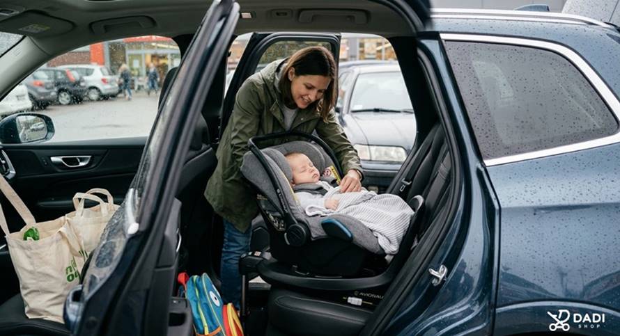 Mama wygodnie układa śpiące niemowlę w foteliku zamontowanym na bazie obrotowej w samochodzie podczas zakupów.